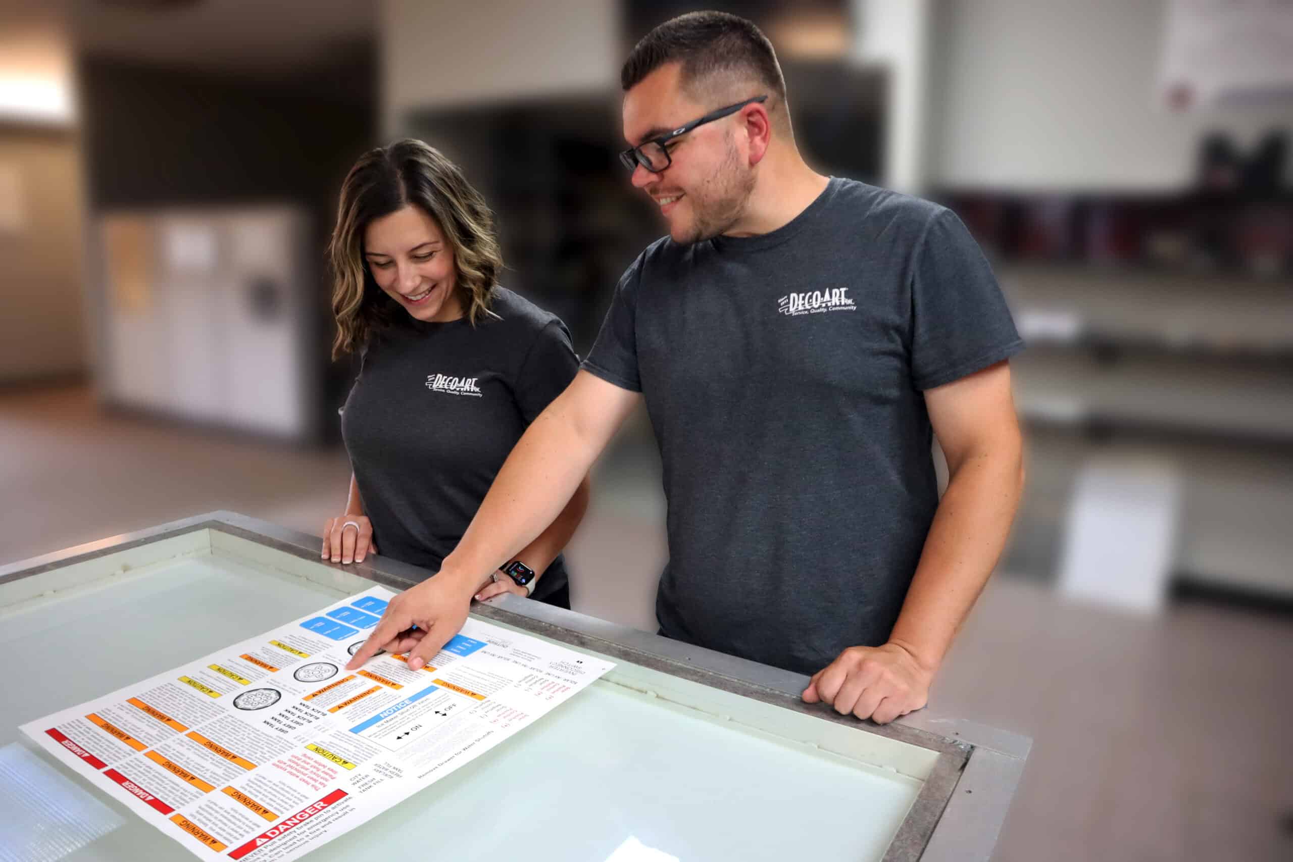 Man and woman standing at a light table with man pointing to a label on a label sheet